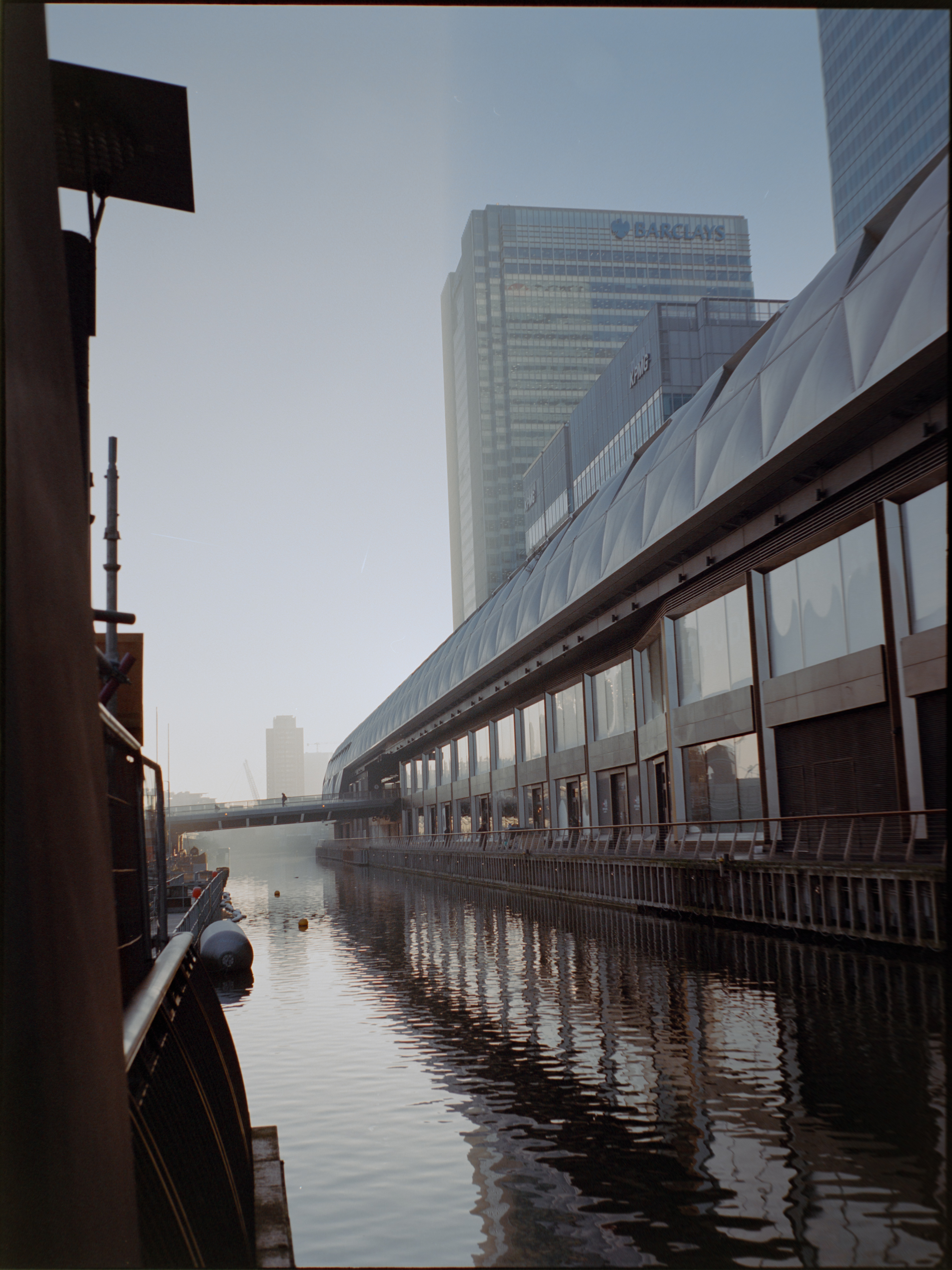 Person on walkway bridge with modern Canary Wharf buildings — candid street photography on medium format film