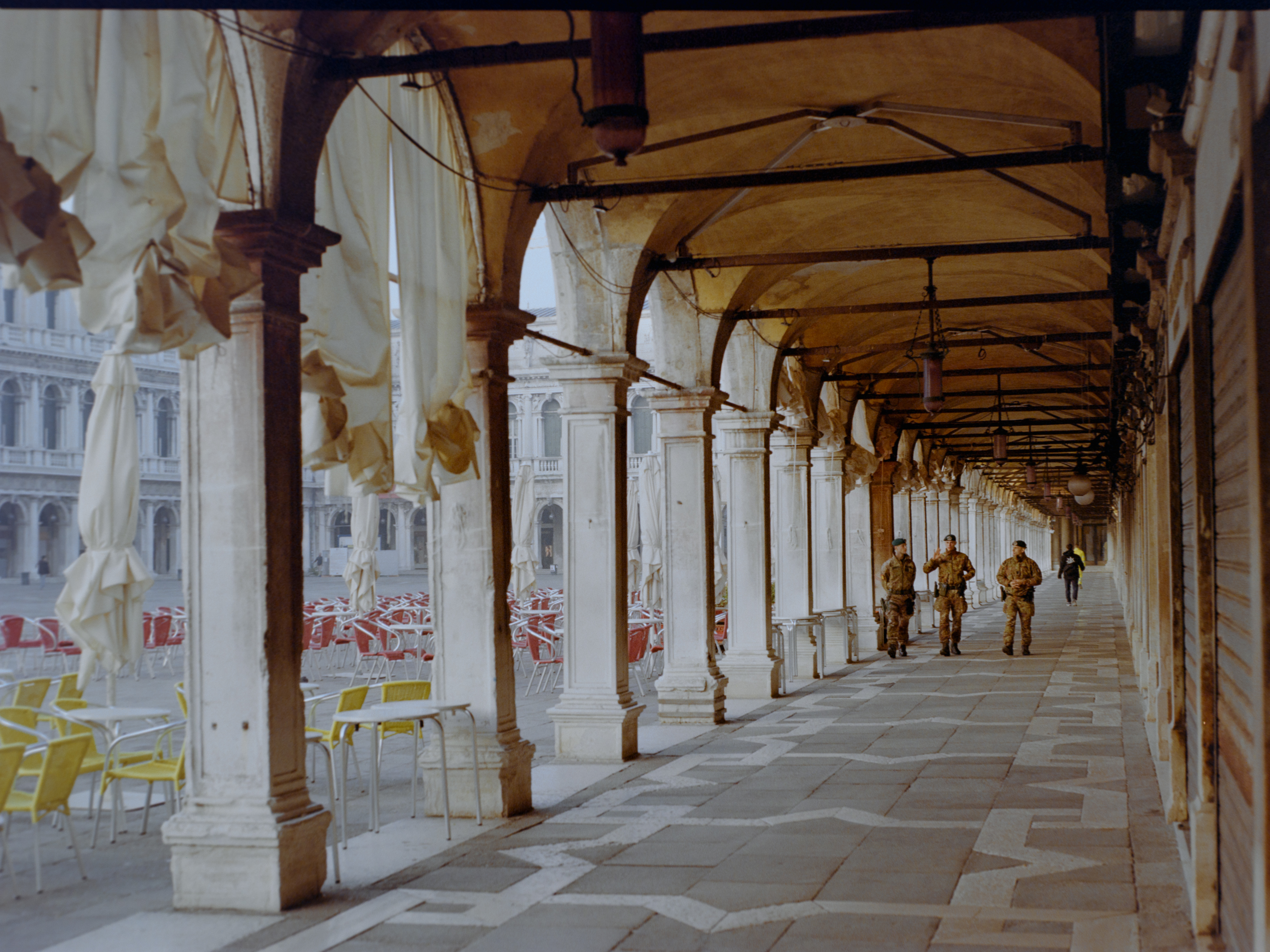 Colonnade with uniformed figures walking through furled canvas awnings — Venice on Kodak Gold 200