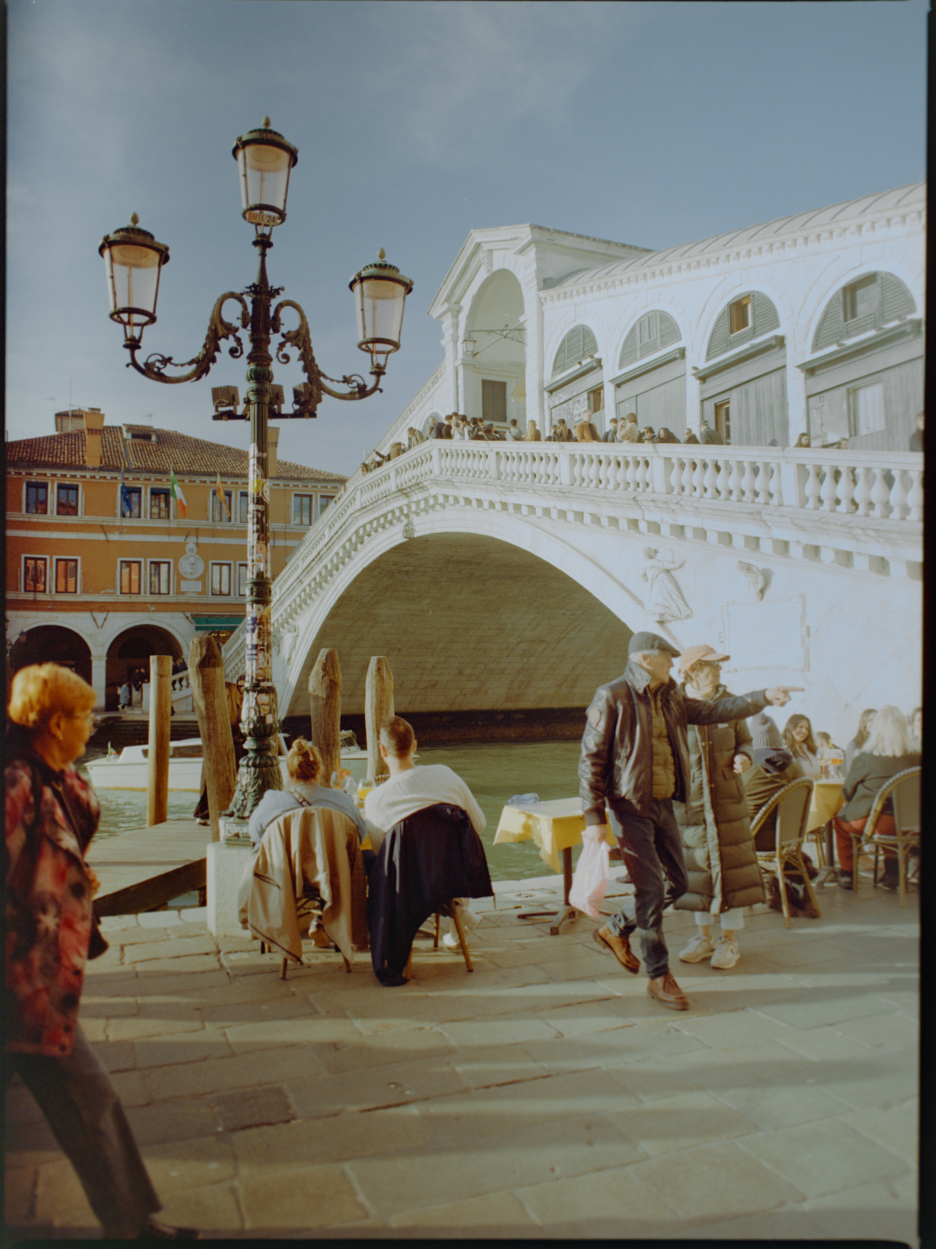Street-level view looking up at the Rialto Bridge with cafe diners in the foreground — Venice on Gold 200