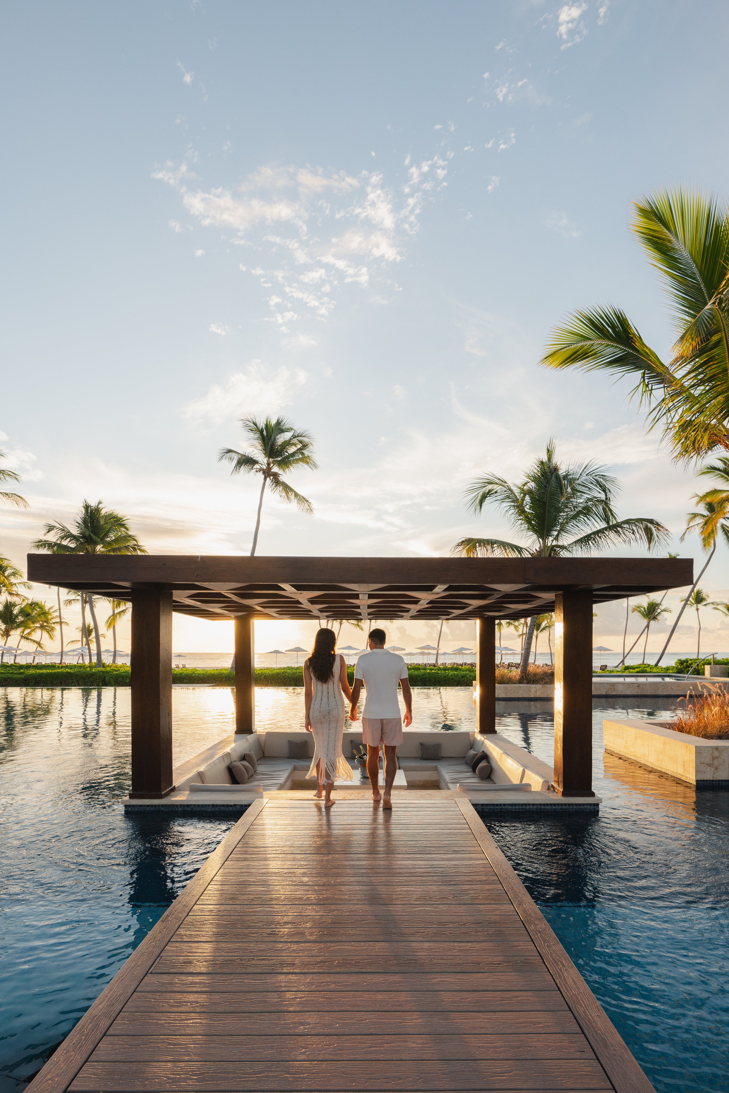couple infinity pool sunrise tropical resort palm trees