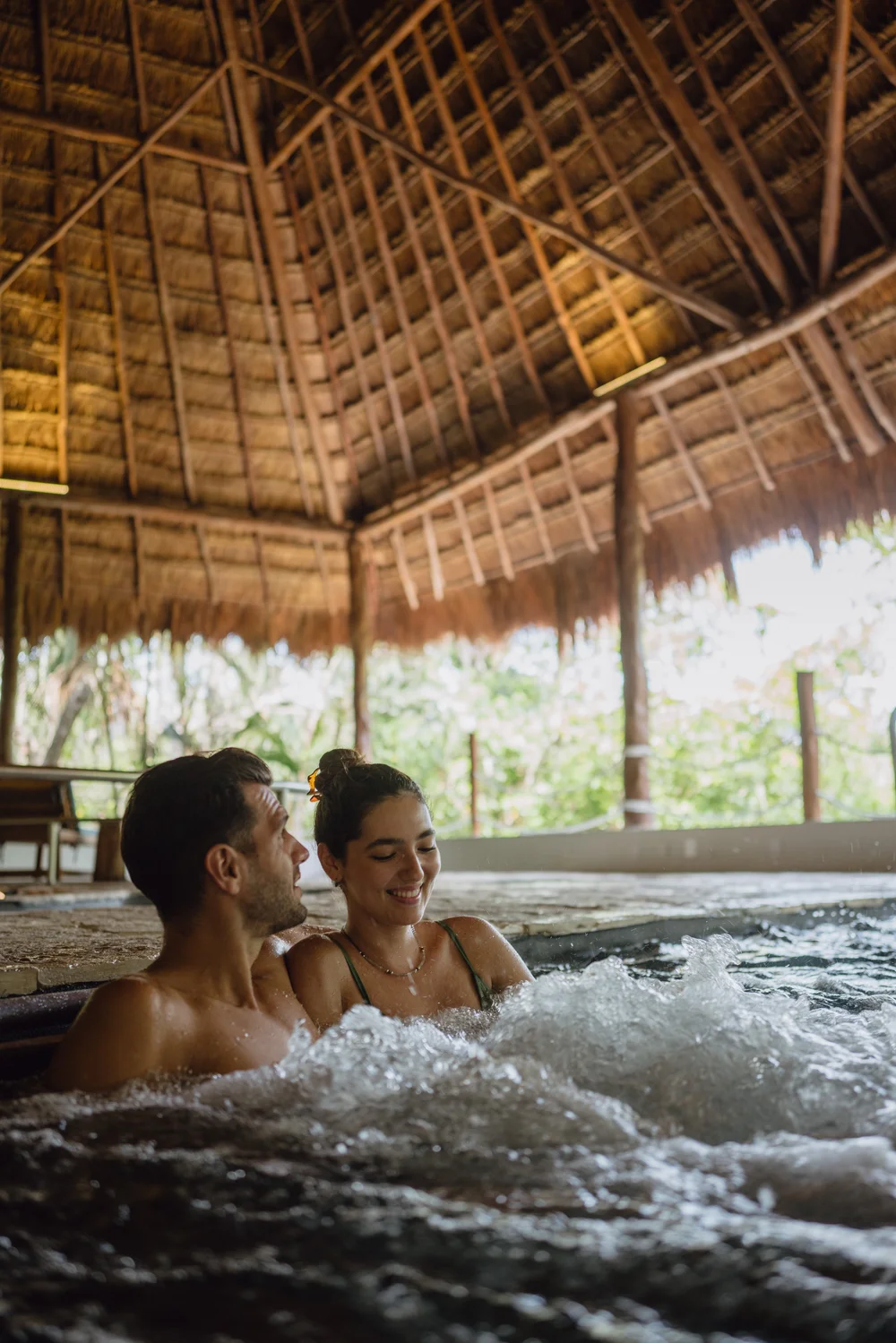 Couple laughing in outdoor jacuzzi hydrotherapy thatched palapa roof Riviera Maya
